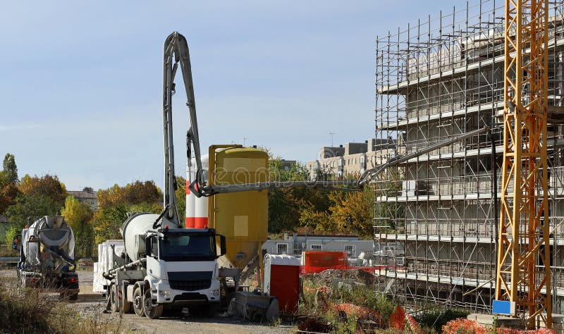 Cement mixer trucks at work on a facade under construction covered with scaffoldings