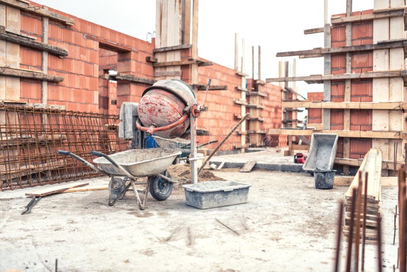 Cementowego melanżeru maszyna przy budową, narzędziami, wheelbarrow, piaskiem i cegłami przy domowym budynkiem