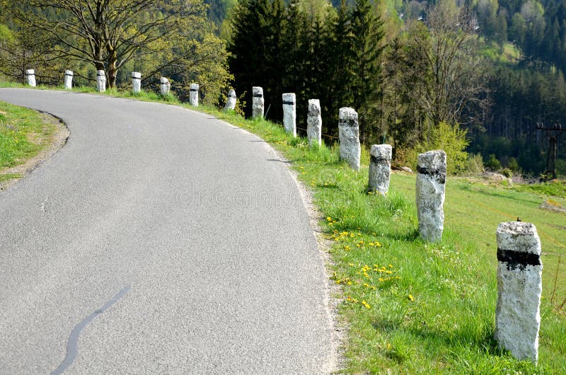 Granite stone bollards old line the mountain road at the moat on the edge of the white curb with a black stripe in a row turn