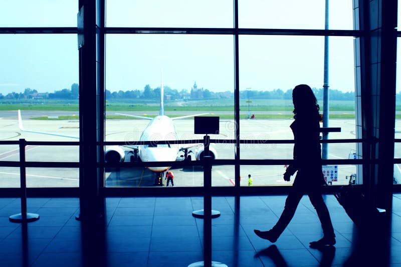 Classic airport scene with woman carrying luggage in the airport departure gate, plane parked at the gate in background. Classic airport scene with woman carrying luggage in the airport departure gate, plane parked at the gate in background