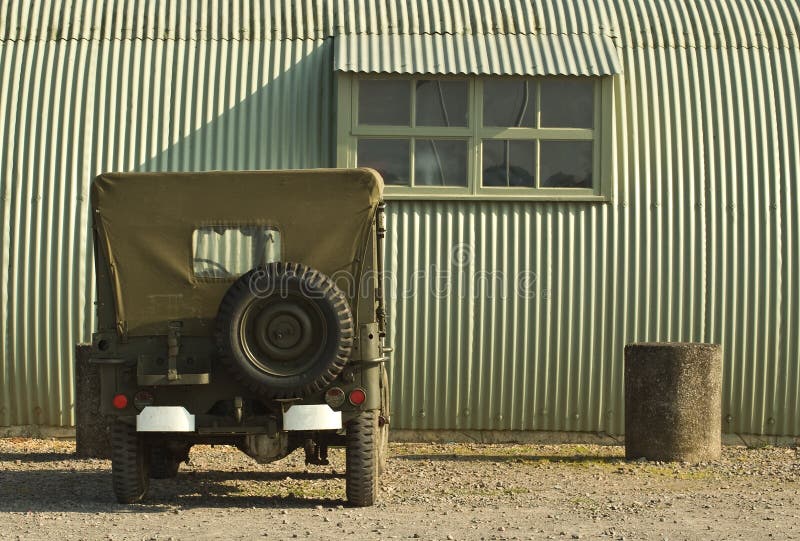 A wartime jeep is parked outside a period military building. A wartime jeep is parked outside a period military building