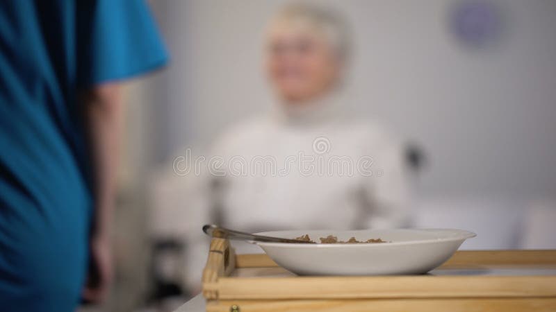 Cena joven de la porción de la enfermera a la vieja señora perjudicada, tomando cuidado sobre paciente