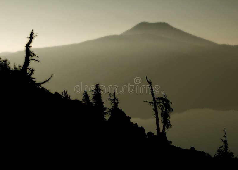 Ghostly tree remnants silhouetted against smoke filled sky due to nearby forest fire at rim of Crater Lake, Oregon. Ghostly tree remnants silhouetted against smoke filled sky due to nearby forest fire at rim of Crater Lake, Oregon