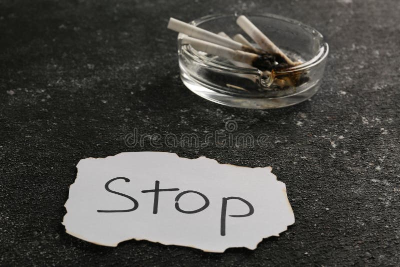 Ashtray with burnt cigarettes and word Stop written on paper on black textured table. No smoking concept. Ashtray with burnt cigarettes and word Stop written on paper on black textured table. No smoking concept