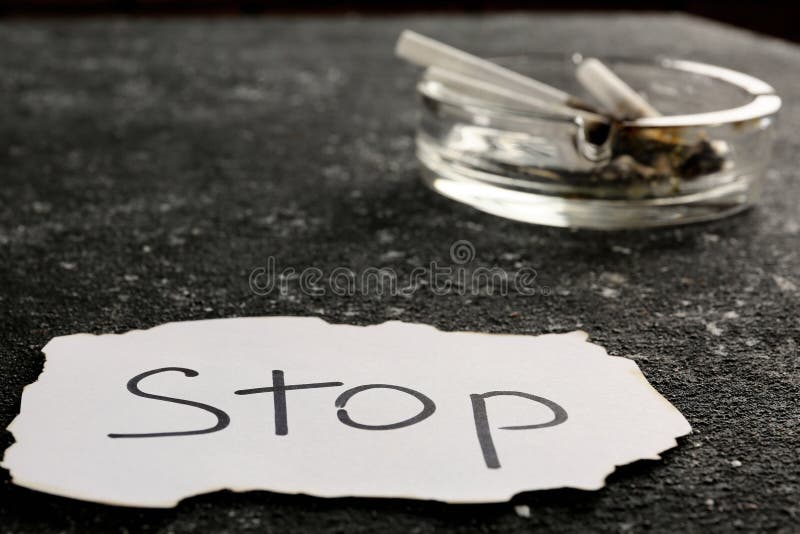 Ashtray with burnt cigarettes and word Stop written on paper on black textured table. No smoking concept. Ashtray with burnt cigarettes and word Stop written on paper on black textured table. No smoking concept