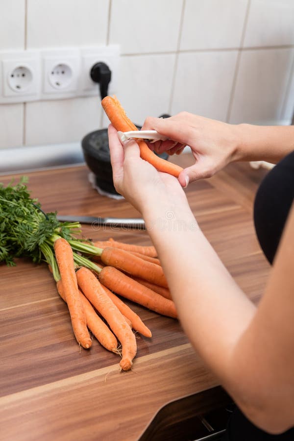 Cenouras da casca da mulher na cozinha fotografia de stock Cenouras da casca da mulher na cozinha fotografia de stock