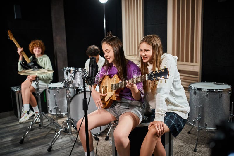 focus on teenage girls with guitar singing with blurred friends with drums and guitar on backdrop, stock photo. focus on teenage girls with guitar singing with blurred friends with drums and guitar on backdrop, stock photo