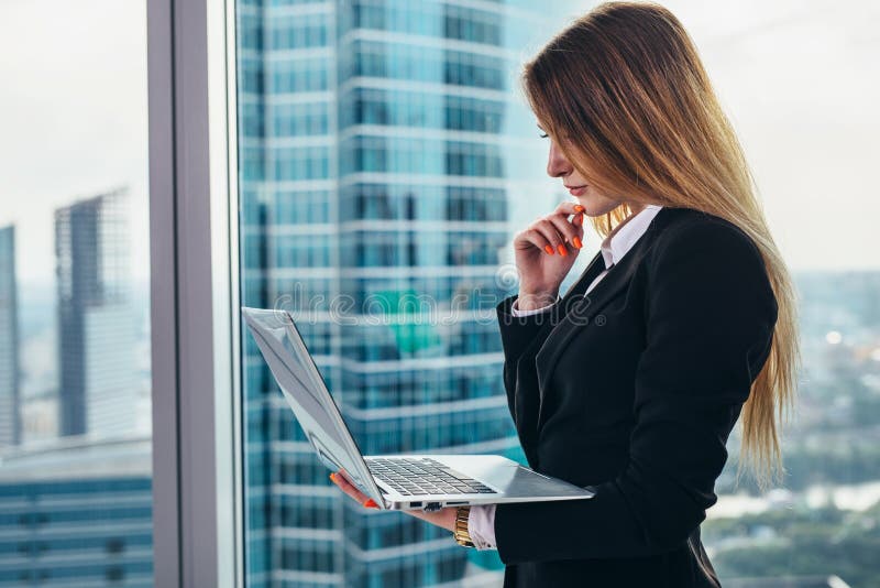 CEO femminile premuroso che sta contro la finestra nel suo ufficio privato nel centro di affari moderno che tiene una lettura del immagine stock CEO femminile premuroso che sta contro la finestra nel suo ufficio privato nel centro di affari moderno che tiene una lettura del immagine stock