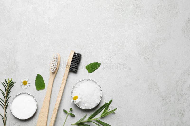 Cepillos de dientes de bambú flores y hierbas sobre mesa gris claro estría plana. espacio para texto