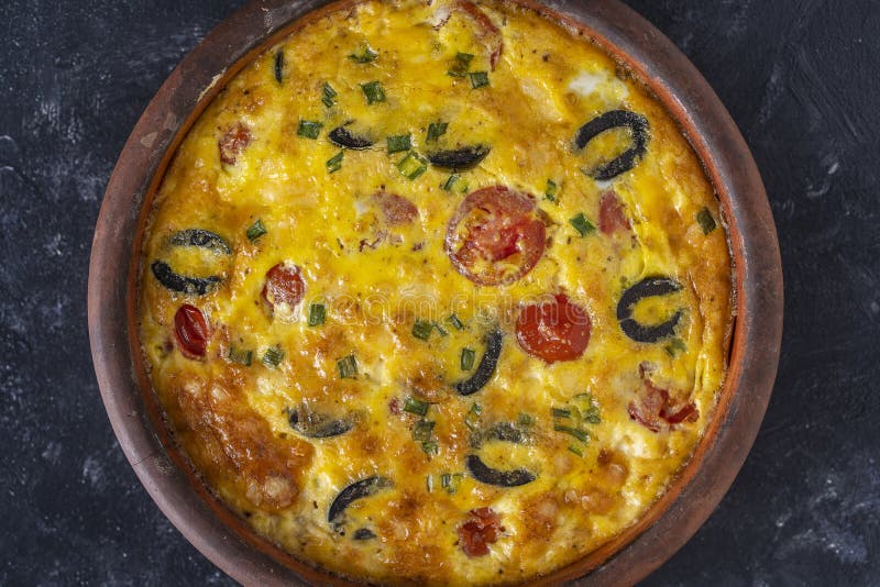 Frittata with egg, pepper, onion, olives, tomato and cheese on table. Italian egg omelette