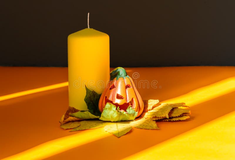 Ceramic Halloween pumpkin jack-o-lantern on dry autumn leaves, yellow candle and strong shadows stock photo