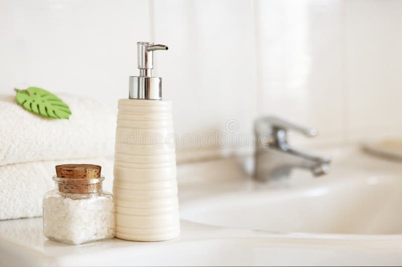 Ceramic soap, shampoo bottle, glass bottle with bath salt and white cotton towels on Blurred bathroom interior background with