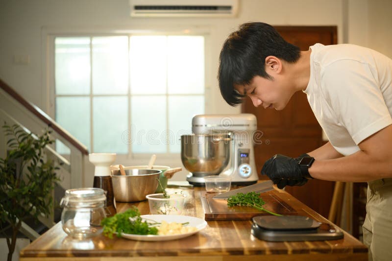 Cerca de un hombre cortando hierbas frescas preparando ingredientes en una cocina de casa fotos de archivo