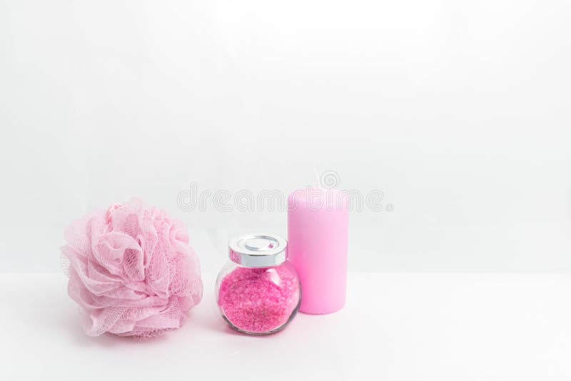 Cerca hay un frasco de sal de baño, una esponja para el baño y una vela. objetos rosa claro sobre un fondo blanco. el. Un frasco transparente con sal de baño con una tapa metálica, una esponja para el baño y un puesto de vela cerca sobre un fondo blanco. todos los objetos tienen un color rosa claro. el concepto de ducha, cuidados personales y spa. foto horizontal.