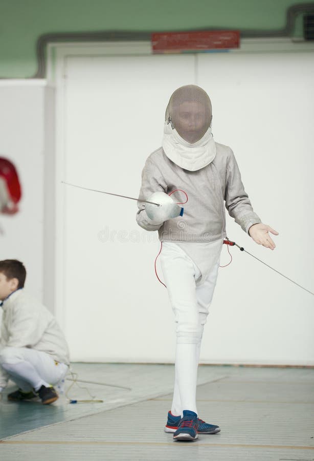 Cercador del adolescente del muchacho en traje especial en la competencia de cercado con el estoque en la posición que lucha fotos de archivo Cercador del adolescente del muchacho en traje especial en la competencia de cercado con el estoque en la posición que lucha fotos de archivo