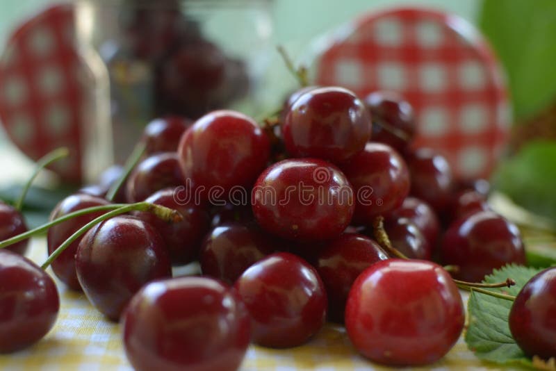 Cerejas vermelhas na toalha de mesa amarela e no tampão vermelho dos frascos foto de stock Cerejas vermelhas na toalha de mesa amarela e no tampão vermelho dos frascos foto de stock