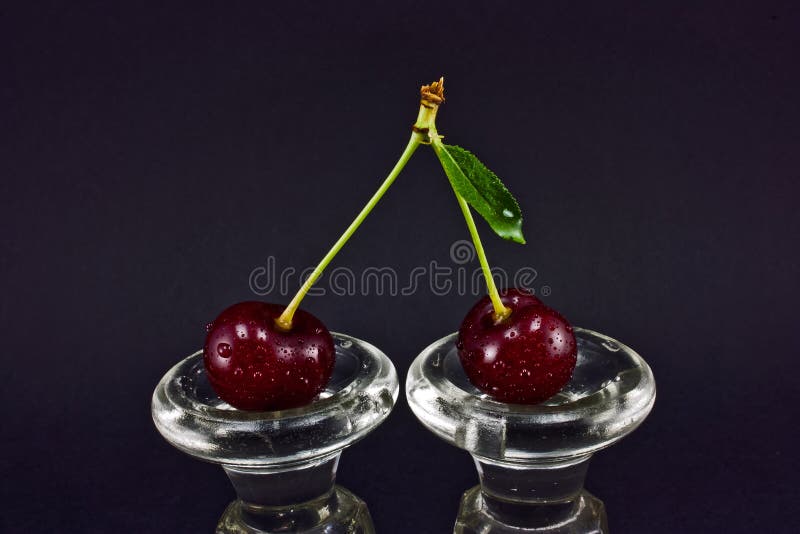 Two cherries on a glass base and a black background. Two cherries on a glass base and a black background