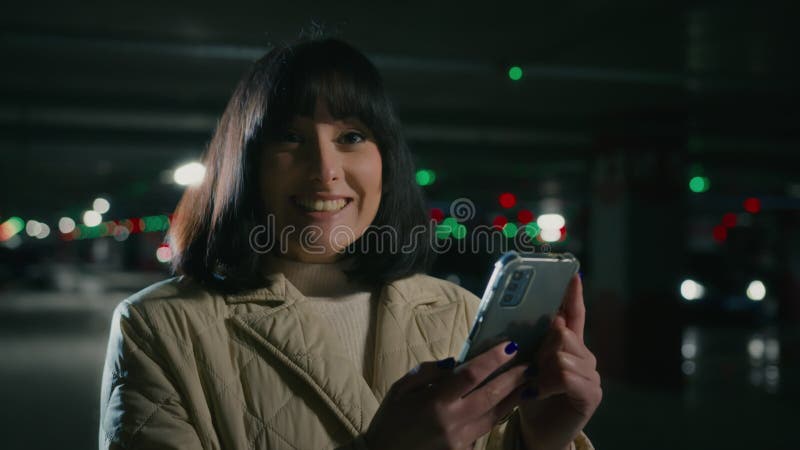 Cerrar feliz impactada mujer sorprendida con teléfono en estacionamiento oscuro ganar logro triunfo en línea con