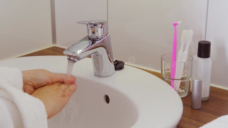 Cerrar la mano femenina en el cuarto de baño lavar las manos bajo el agua corriente en el concepto de lavabo de cerámica blanca de