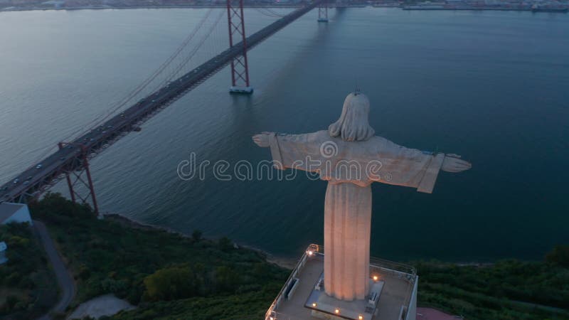 Cerrar la órbita aérea del gran monumento blanco de santuario de cristo rei y el ponte rojo 25 de abril bridge frente a la costa metrajes
