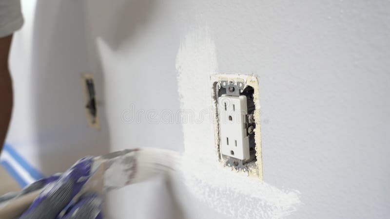 Cerrar las manos del pintor con guantes pintando la pared alrededor de la toma de corriente almacen de metraje de vídeo