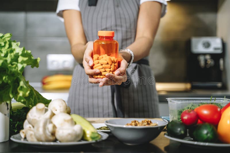 Close up of female hands holding nutritional supplements or vitamins in the kitchen. Choice, balanced diet and health concept. Close up of female hands holding nutritional supplements or vitamins in the kitchen. Choice, balanced diet and health concept.