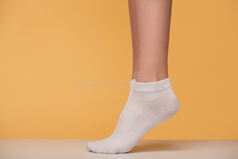 Women`s legs in white socks close-up. Yellow background. Women`s legs in white socks close-up. Yellow background