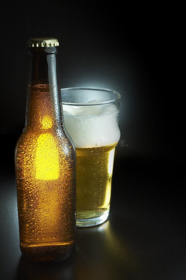 Cold unopened bottle of beer near a frothy beer pint. Cold unopened bottle of beer near a frothy beer pint