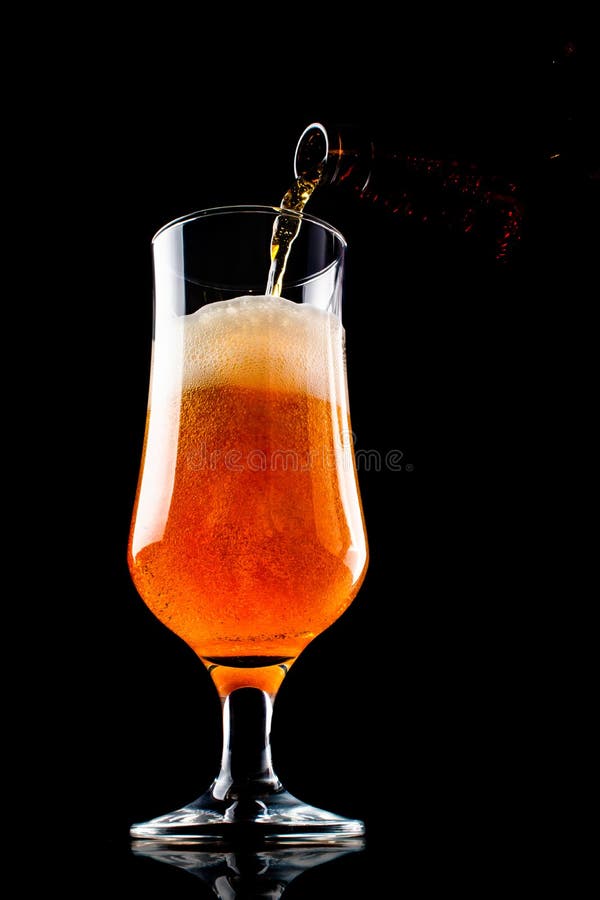 A cerveja está derramando em um vidro da garrafa no fundo preto fotos de stock royalty free A cerveja está derramando em um vidro da garrafa no fundo preto fotos de stock royalty free