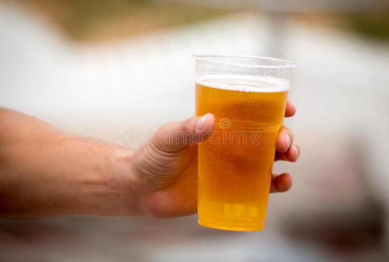 Cerveja fresca em um copo plástico na mão imagem de stock Cerveja fresca em um copo plástico na mão imagem de stock