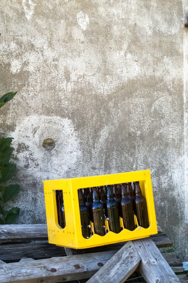 Cerveja vazia escura Bootle na caixa amarela do caso nas partes de madeira na parte externa na frente da parede do cimento fotografia de stock royalty free Cerveja vazia escura Bootle na caixa amarela do caso nas partes de madeira na parte externa na frente da parede do cimento fotografia de stock royalty free