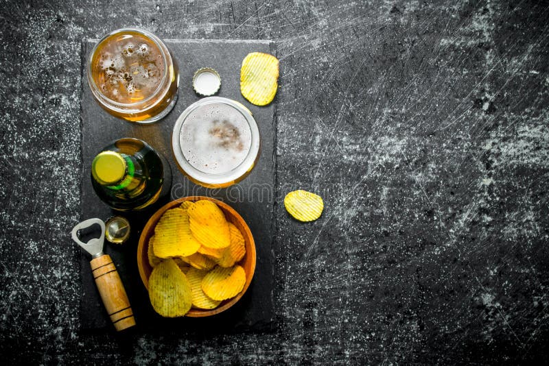 Cerveza con los microprocesadores y abrelatas en la tabla de cortar En fondo r? stico negro