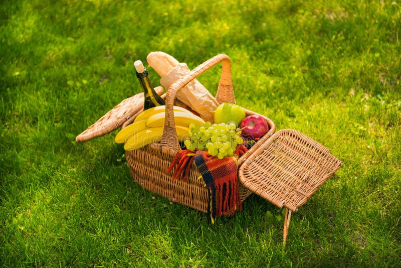 Cesta de mimbre de la comida campestre con las frutas frescas, la botella de vino, el baguette y la tela escocesa en prado verde fotografía de archivo libre de regalías Cesta de mimbre de la comida campestre con las frutas frescas, la botella de vino, el baguette y la tela escocesa en prado verde fotografía de archivo libre de regalías