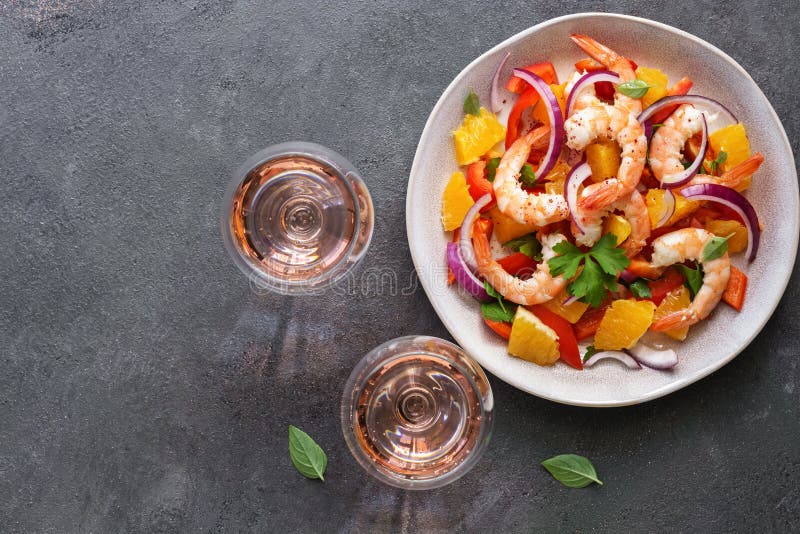 Ceviche with shrimps and orange, two glasses of pink sparkling wine, dark rustic background. Top view, copy space.