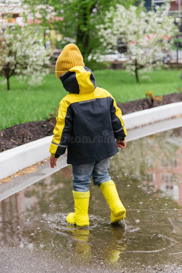 Little boy walks through the puddles in the spring after the rain. Cute baby walks through the puddles in the spring in the city