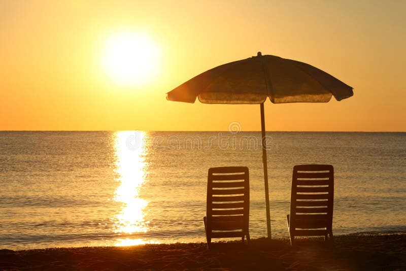 Chairs stand on beach under opened umbrella