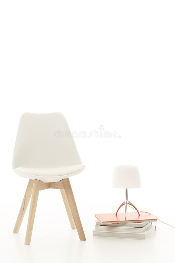 Single stylish modern white chair with a stylish white lamp standing on a stack of hardcover books alongside. Single stylish modern white chair with a stylish white lamp standing on a stack of hardcover books alongside