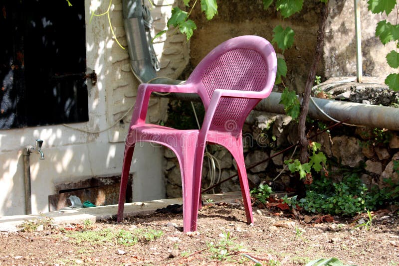 Chaise en plastique d'arrière-cour avec la couleur rose foncée fanée entourée avec le tuyau traditionnel de mur en pierre et de g photo stock Chaise en plastique d'arrière-cour avec la couleur rose foncée fanée entourée avec le tuyau traditionnel de mur en pierre et de g photo stock