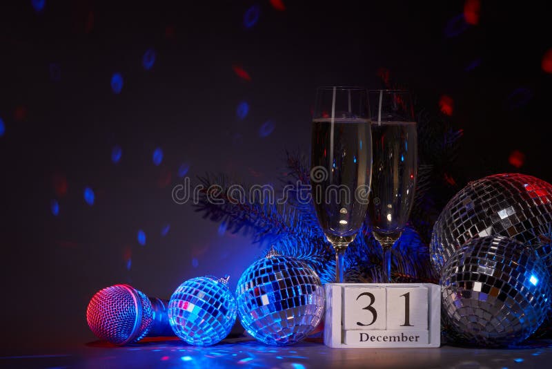 Champagne flutes, mirror balls disco ball, fir branch, microphone  on dark background with blue red lighting. Copy space. New Year. 31 december. Weekend or holiday party.  Karaoke, club, bar. Champagne flutes, mirror balls disco ball, fir branch, microphone  on dark background with blue red lighting. Copy space. New Year. 31 december. Weekend or holiday party.  Karaoke, club, bar