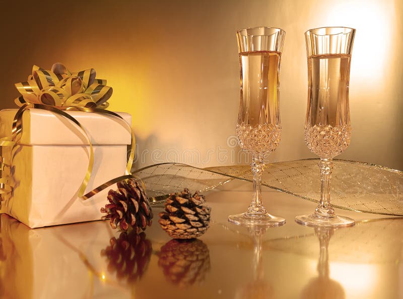Champagne glasses with present gold bow pine cones gold ribbon on gold background