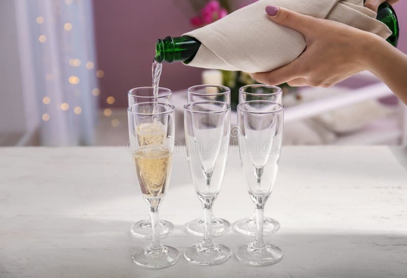 Champagne se renversant de femme de bouteille dans des verres sur la table blanche image libre de droits Champagne se renversant de femme de bouteille dans des verres sur la table blanche image libre de droits