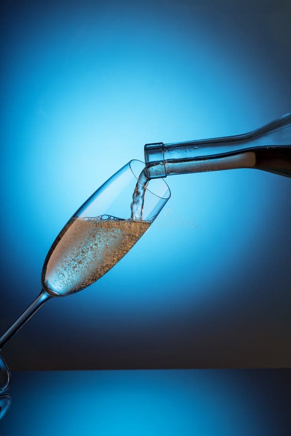 Champagne è versata da una bottiglia in un vetro ruzzolato fotografia stock Champagne è versata da una bottiglia in un vetro ruzzolato fotografia stock