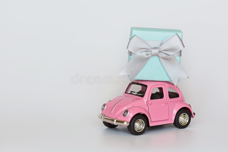 Changxing, China - October 15, 2019: Pink retro toy car delivering gift box on roof on white background. Valentine day February 14