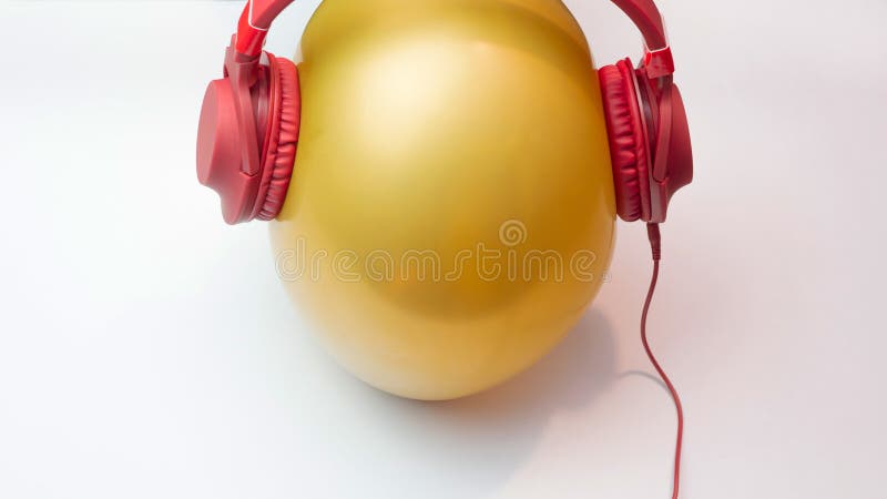 A character in the form of a golden ball listens to music, top view. Red music headphones, music creative copy space background. royalty free stock photo