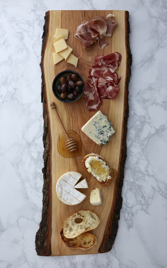 Charcuterie appetizers of meat, cheese, olives, honey and bread on a rustic wood cutting board on a marble surface. Charcuterie appetizers of meat, cheese, olives, honey and bread on a rustic wood cutting board on a marble surface