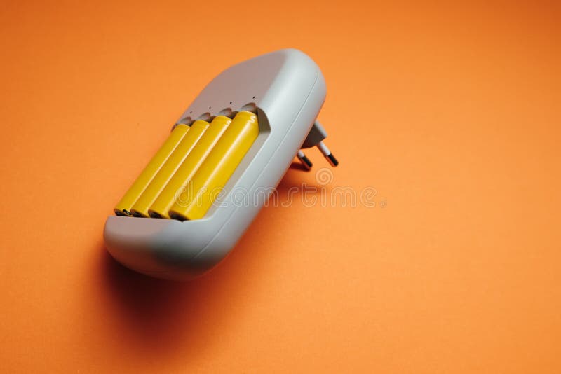 Charger and Batteries. Charger with Yellow AA Accumulator, on Orange