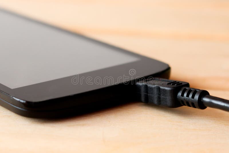 Charging Black Cell Phone On The Background Light Wooden Table Stock