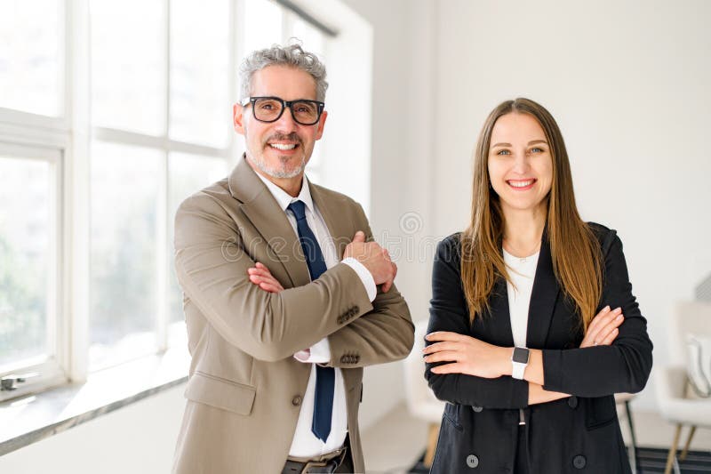 Seasoned businessman with grey hair and a younger female colleague are both stand with arms crossed royalty free stock images