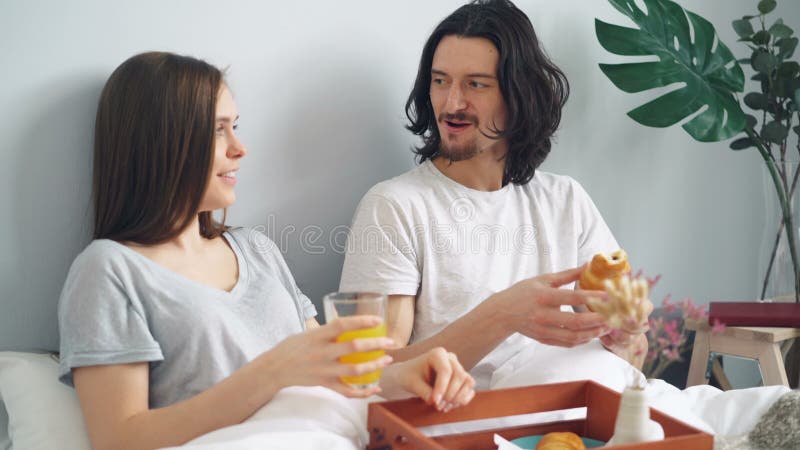 Charla de risa feliz de la gente joven comiendo el desayuno en cama en casa