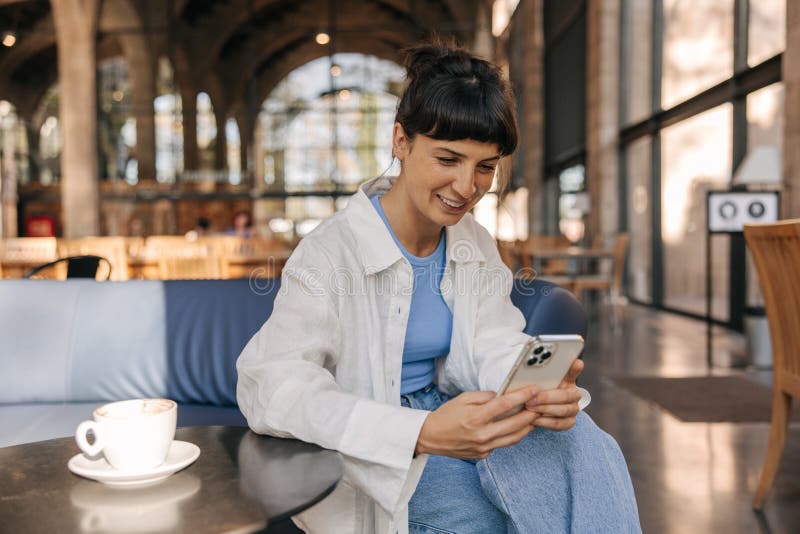 Charmant charmant chic femme assise sur l'entraîneur au café dans le téléphone à main images libres de droits